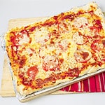 An entire Sicilian rectangular pizza with cheese and tomato topping on a baking sheet