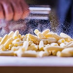 Flour falling over pasta. Falling penne pasta. Rigatoni pasta with flour powder particle falling. Rigatoni Penne Lisce Tortiglioni Doppia Rigatura. Home made rigatoni pasta on the table with flour.