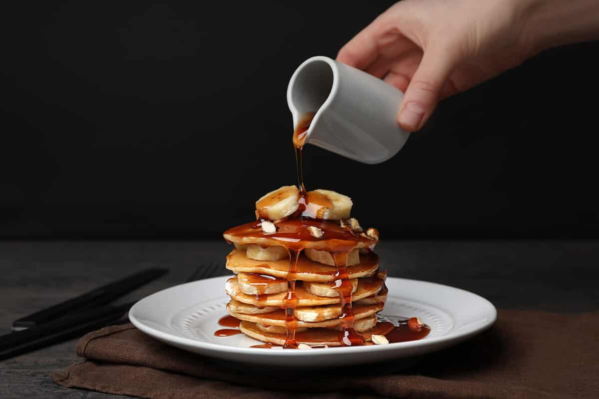 Woman pouring maple syrup on tasty pancakes
