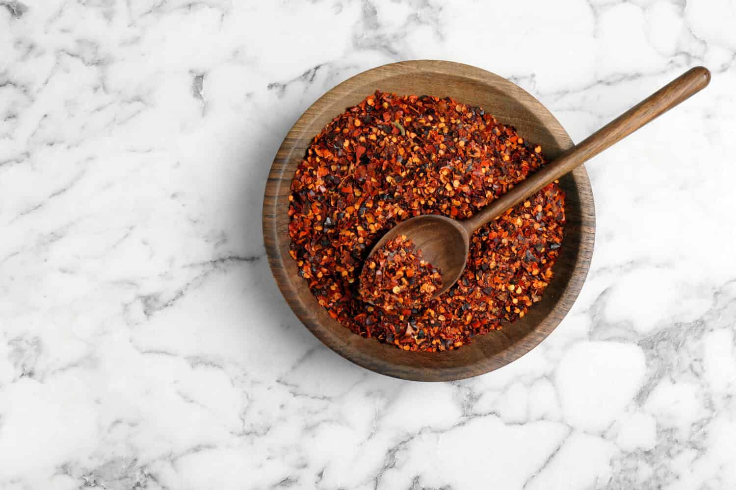 Plate with chili pepper flakes on marble background, top view