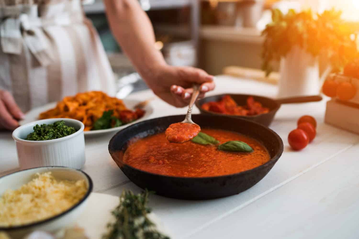 Woman making homemade pasta with tomato sous and cheese over old wooden table. Tomato, olive oil, spices, herbs, cheese, tomato sauce on a weathered wooden table in the summer sun's rays. Organic food