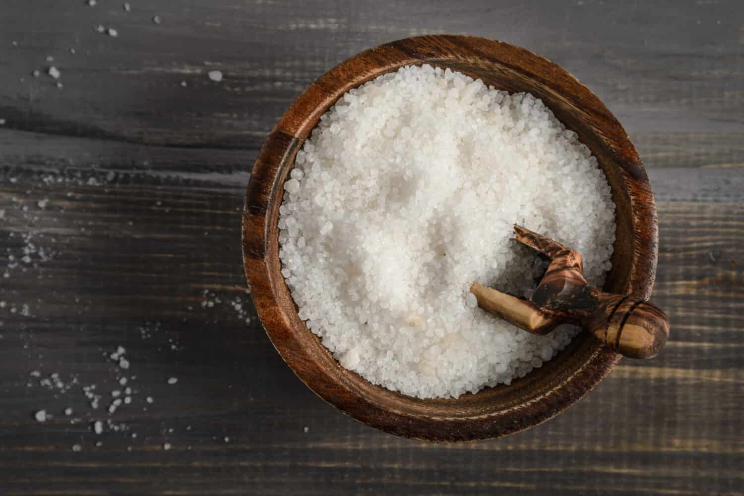 Kosher salt in a wooden bowl with a wooden spoon on a rustic wooden background