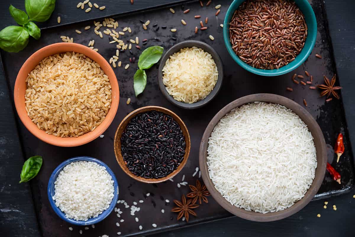 Variety of types and colours of rice - red, black, basmati, whole grain, long grain parboiled and arborio - in bowls. Overhead view