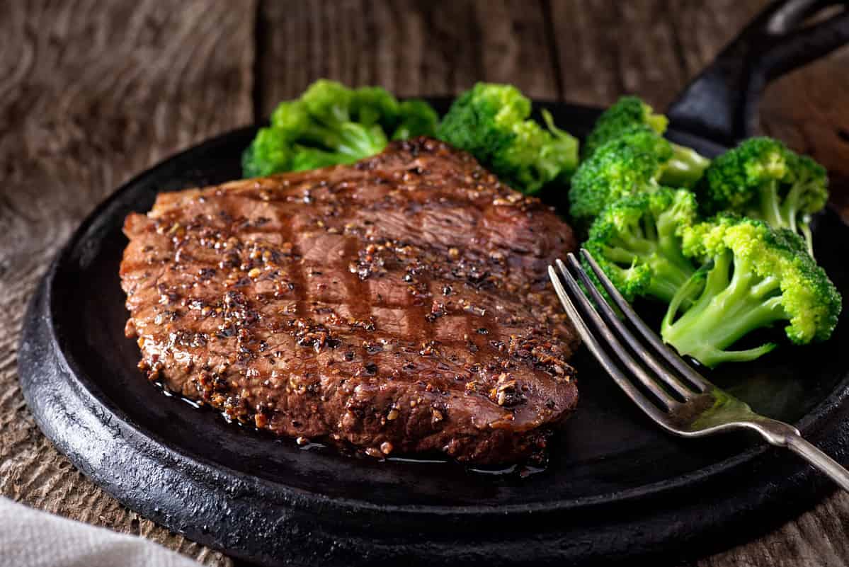A delicious grilled pepper steak with broccoli on a rustic wooden table.