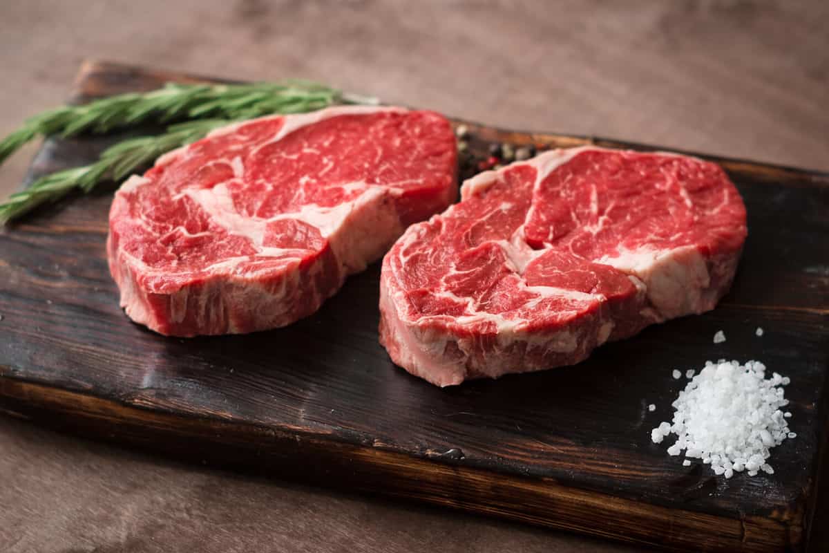 Two fresh raw rib-eye steak on wooden Board on wooden background with salt, pepper and rosmary in a rustic style