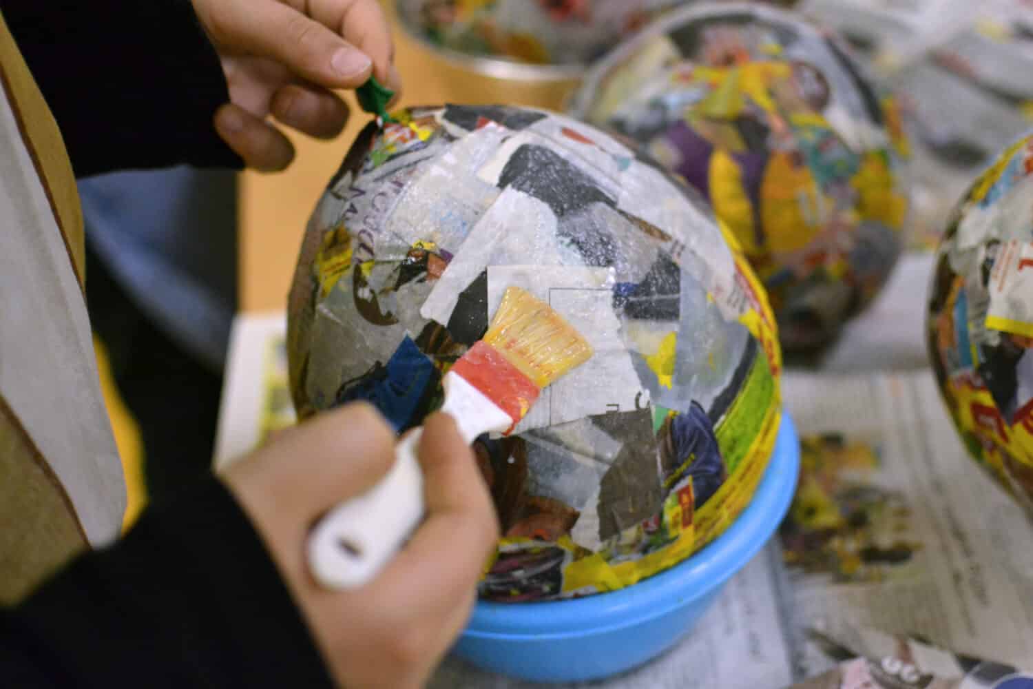 Children hands are making a bowl of paper, glow, balloon and brush.