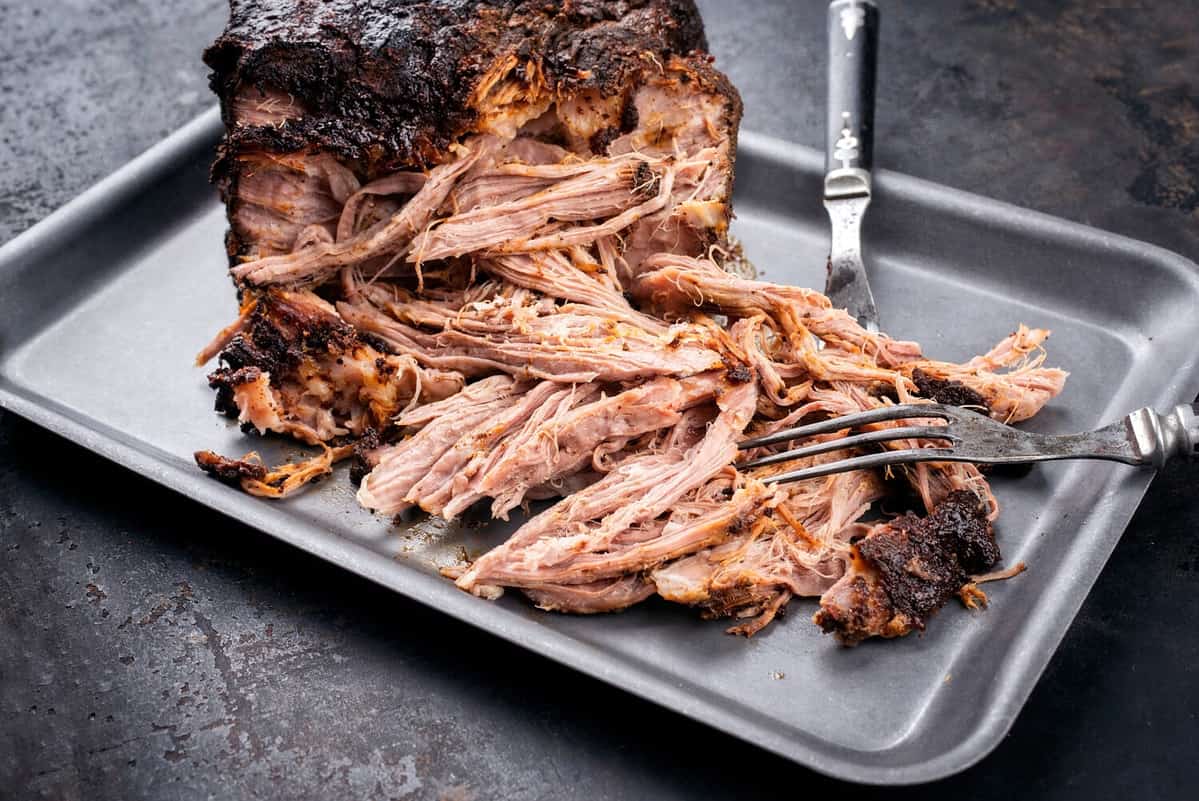 Traditional barbecue pulled pork piece of Bosten butt torn to bits as close-up on a board