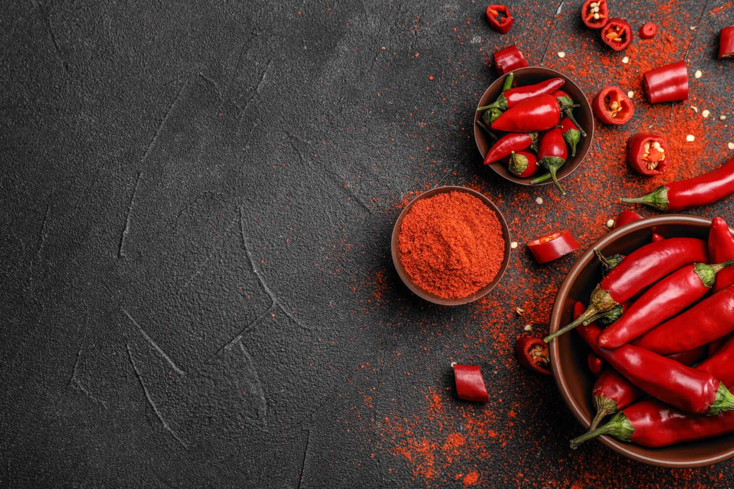 Flat lay composition with powdered and raw chili peppers on dark background. Space for text