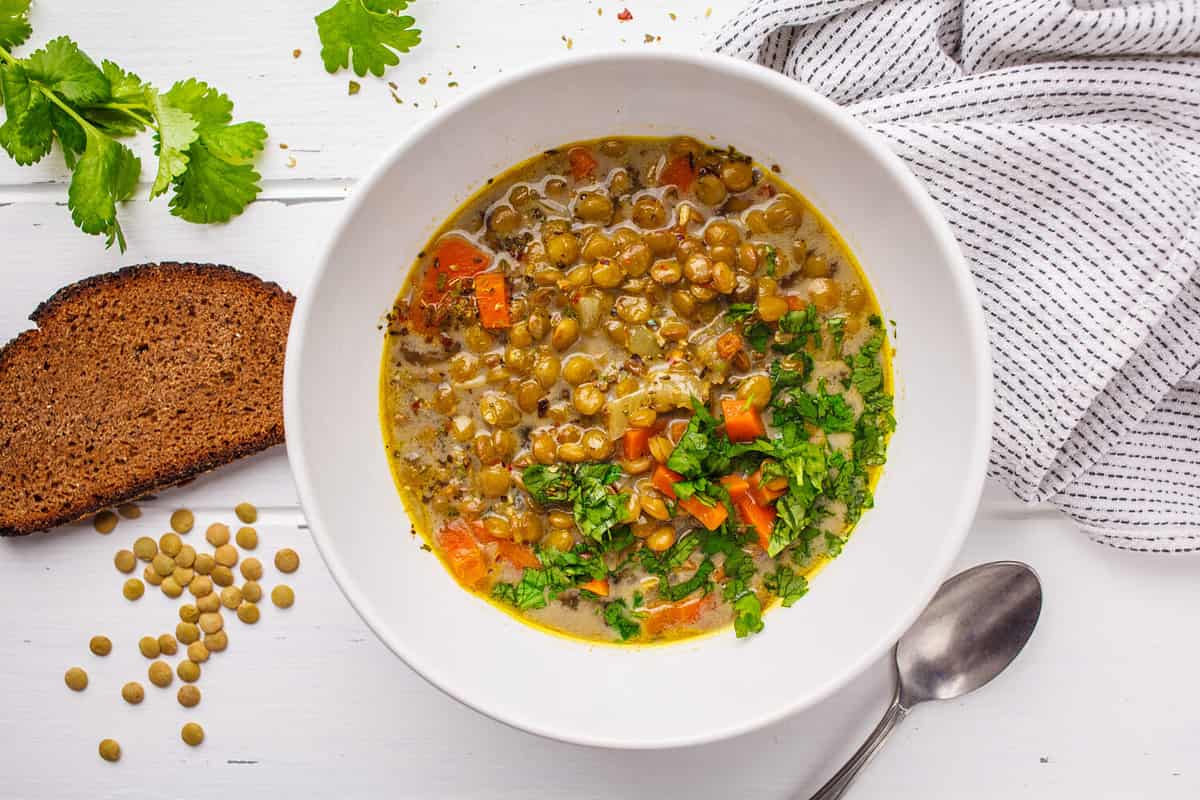 Homemade vegan lentil soup with vegetables and cilantro, white wooden background, top view. Indian vegetarian cuisine.