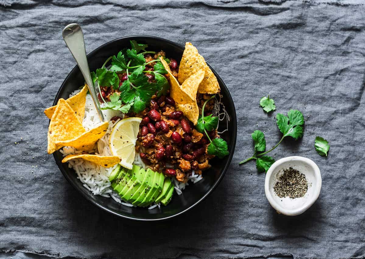 Burrito rice bowl with tortilla chips, cilantro and avocado on grey background, top view