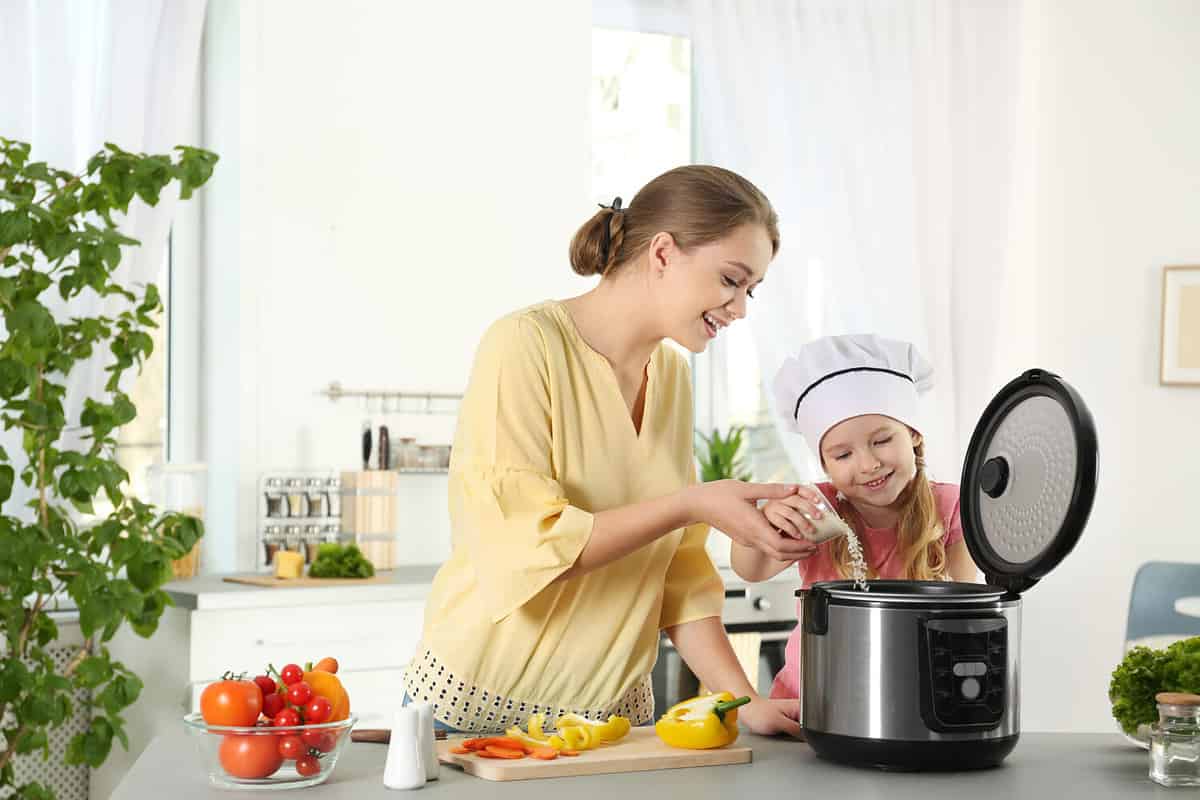 Mother and daughter preparing food with modern multi cooker in kitchen