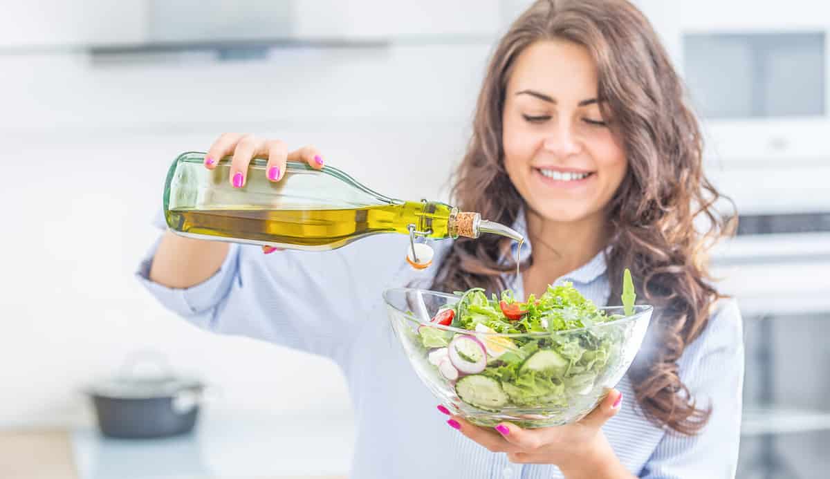 Young woman pouring olive oil in to the salad. Healthy lifestyle eating concept.