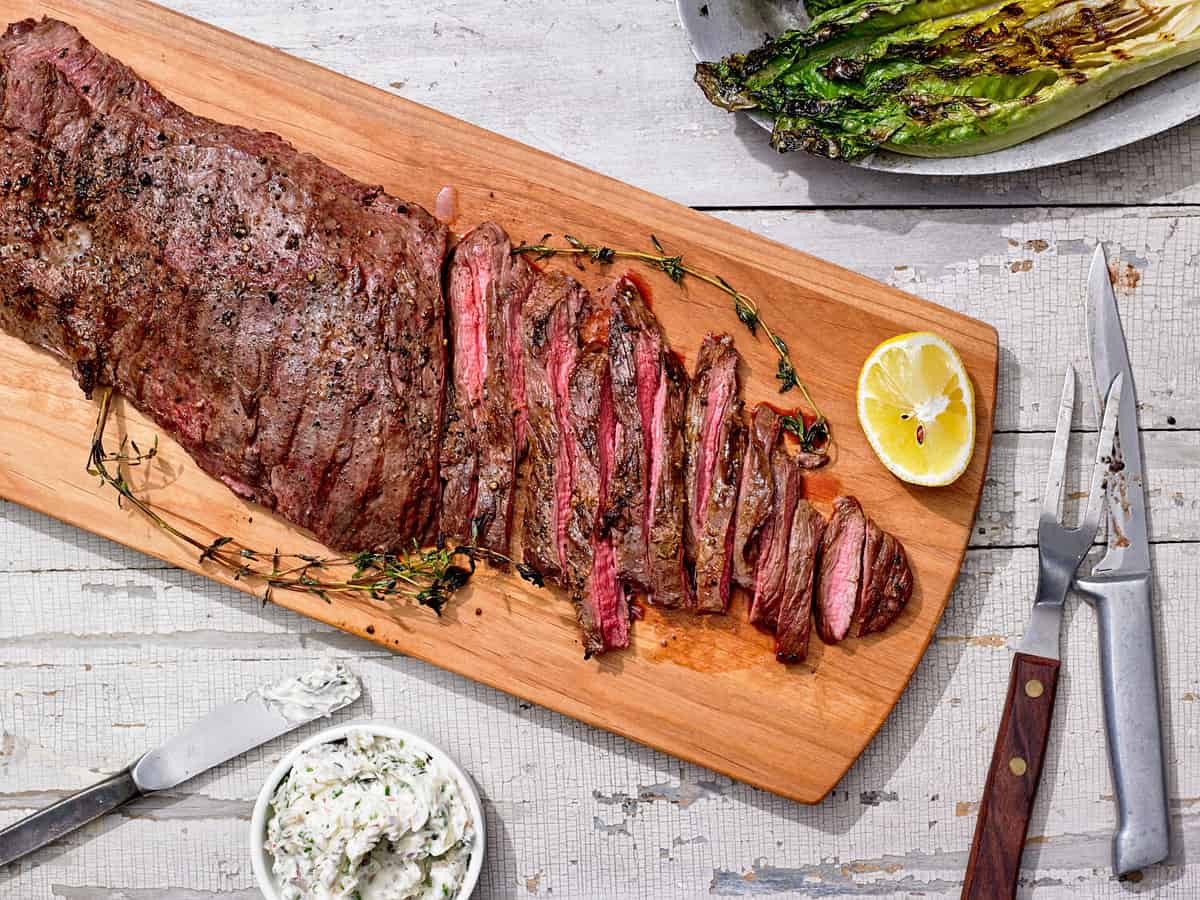 Grilled Skirt Steak sliced with Shallot Thyme Butter and asparagus on cutting board with fork and knife