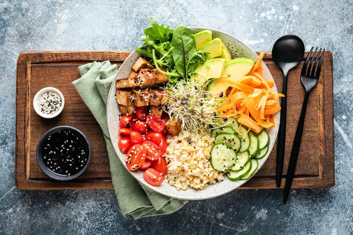 Lifestyle bowl with tofu, avocado, bulgur grains, cucumber, carrot and tomato garnished with seeds and micro greens. Healthy vegan and vegetarian food, tasty lunch or meal. Top view salad bowl