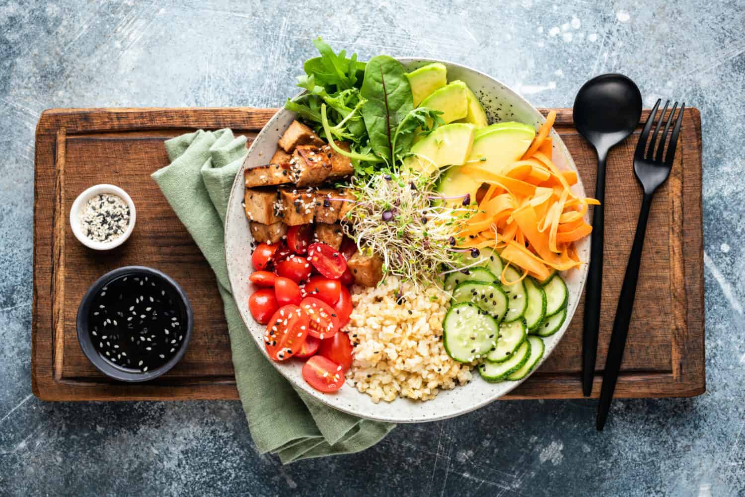 Lifestyle bowl with tofu, avocado, bulgur grains, cucumber, carrot and tomato garnished with seeds and micro greens. Healthy vegan and vegetarian food, tasty lunch or meal. Top view salad bowl