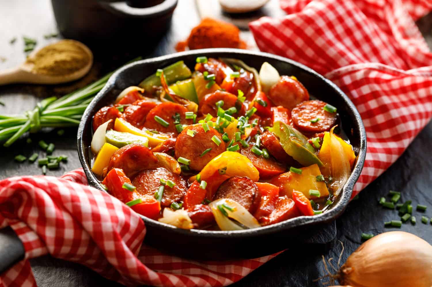 Stew with peppers and sausage in a cast iron skillet on a black background, close up. Traditional Hungarian dish called lecho