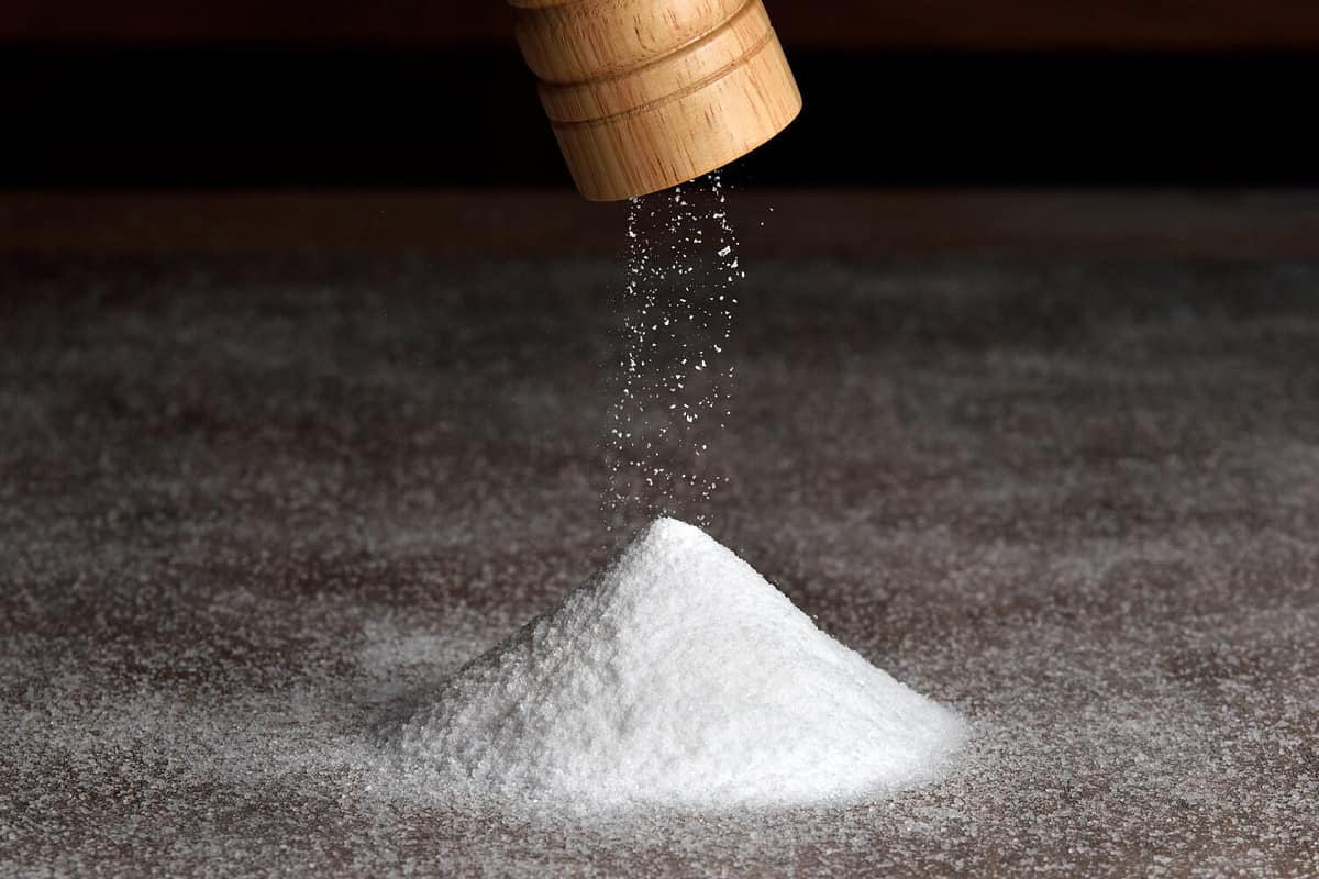 Wooden salt grinder and pile of salt. Salt falls from the grinder on a table full of salt.