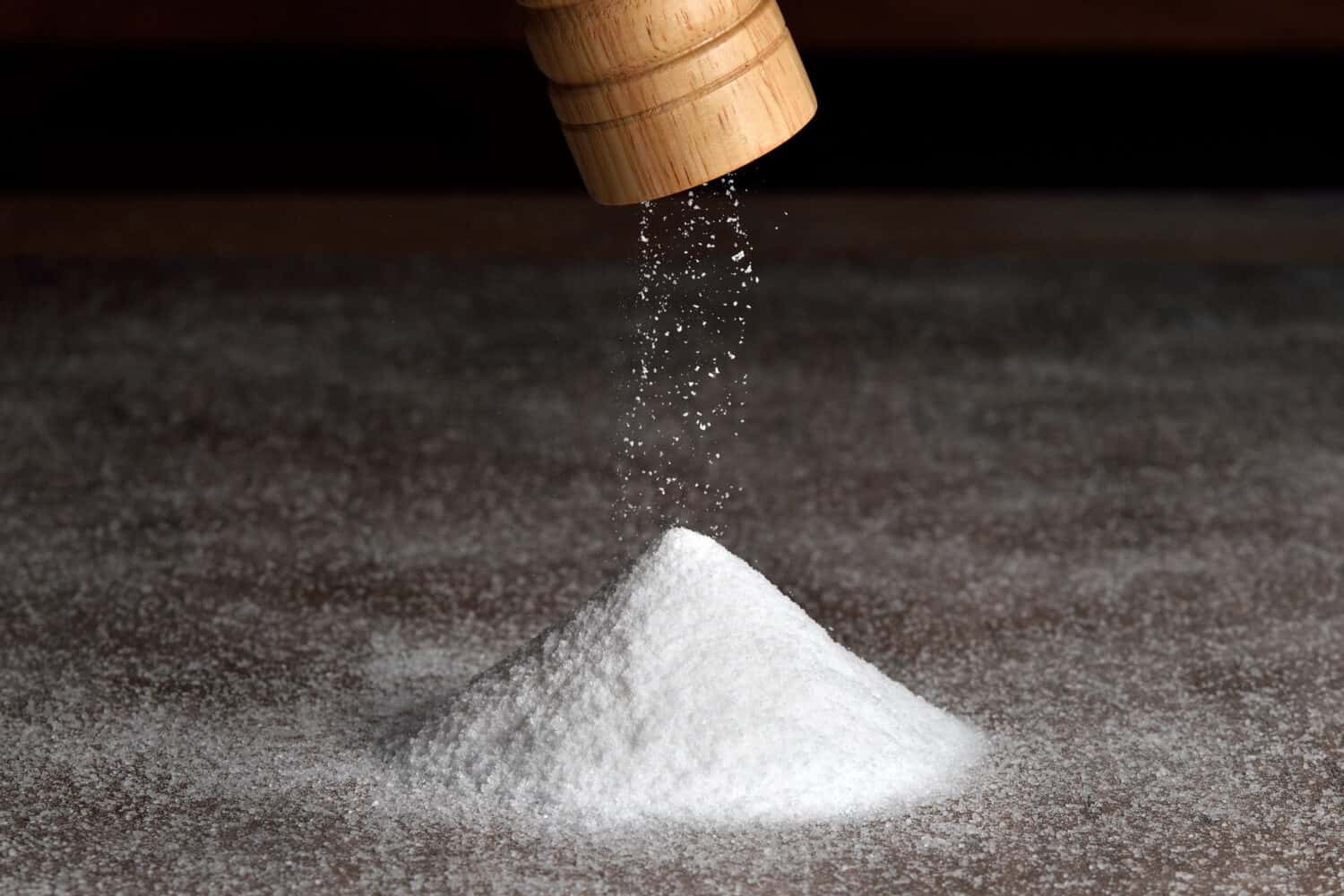 Wooden salt grinder and pile of salt. Salt falls from the grinder on a table full of salt. 