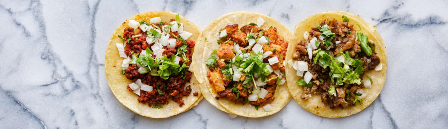 Tostadas vs. Tacos: row of mexican street tacos with carne asada and al pastor in corn tortilla wide banner composition
