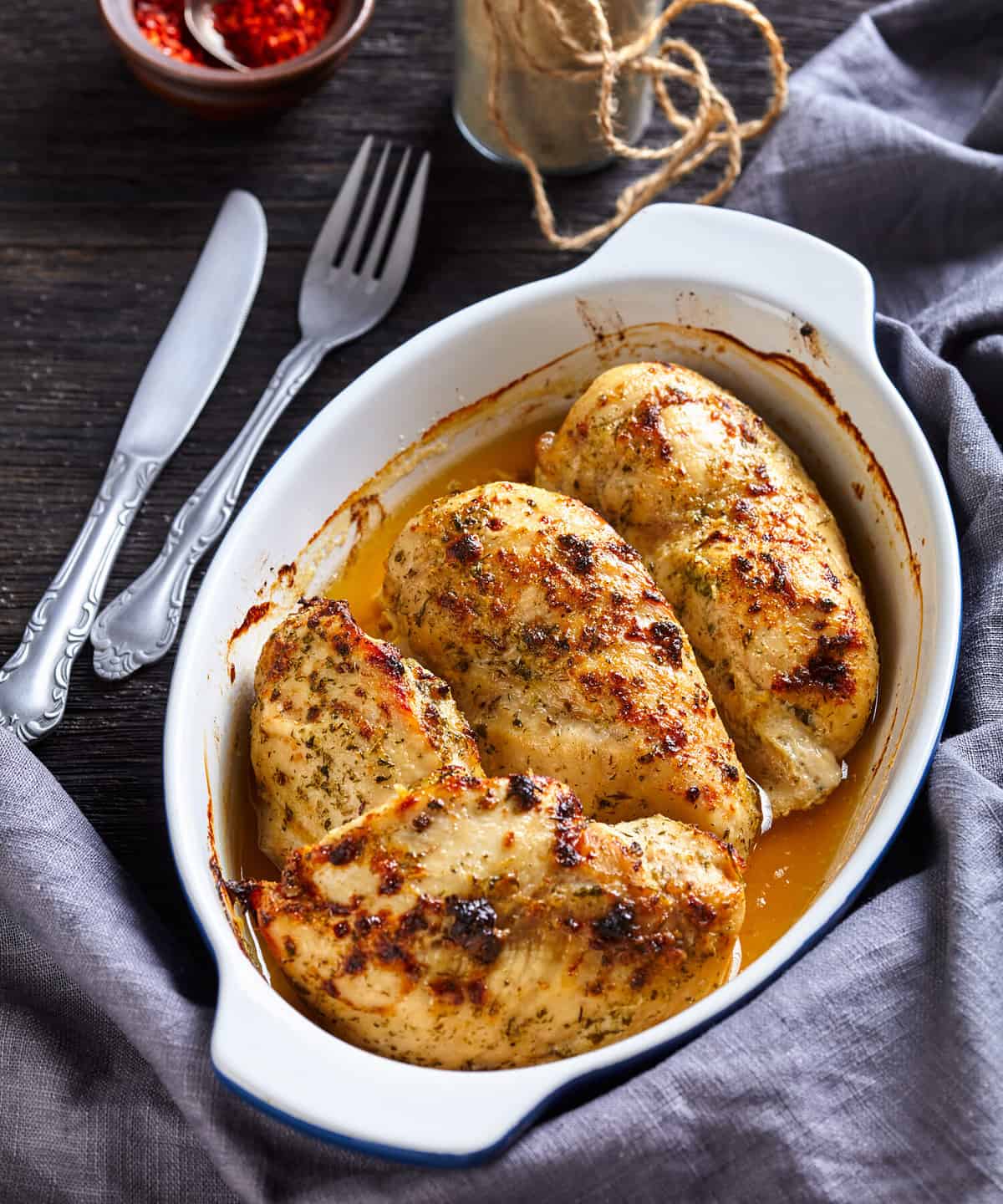 oven baked spicy juicy chicken breasts in a baking dish on a dark wooden table, vertical view from above