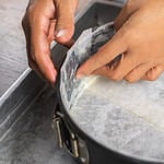 A cake tin line with wax paper and wrap in aluminum foil on a tray for putting a water bath before baking a cheesecake in the oven.