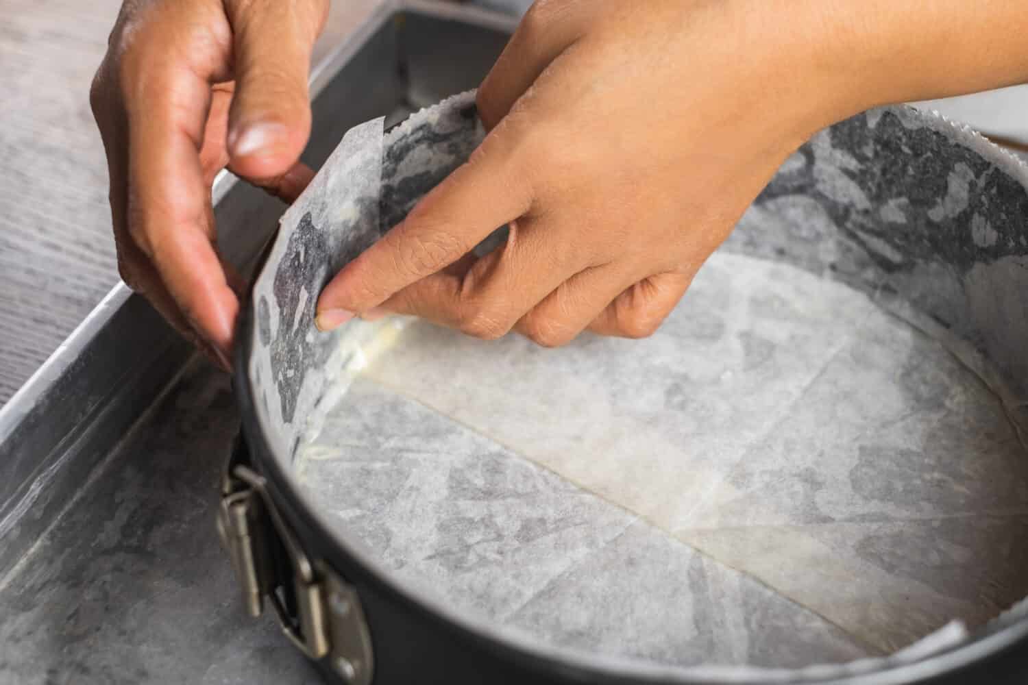 A cake tin line with wax paper and wrap in aluminum foil on a tray for putting a water bath before baking a cheesecake in the oven.