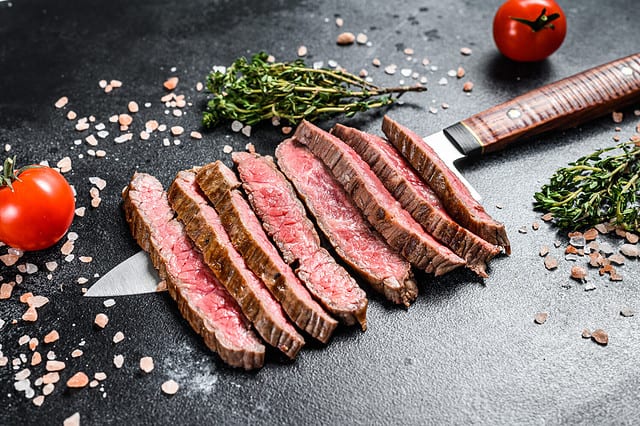 Grilled and sliced flat iron rare steak. Marble beef meat. Black background. Top view