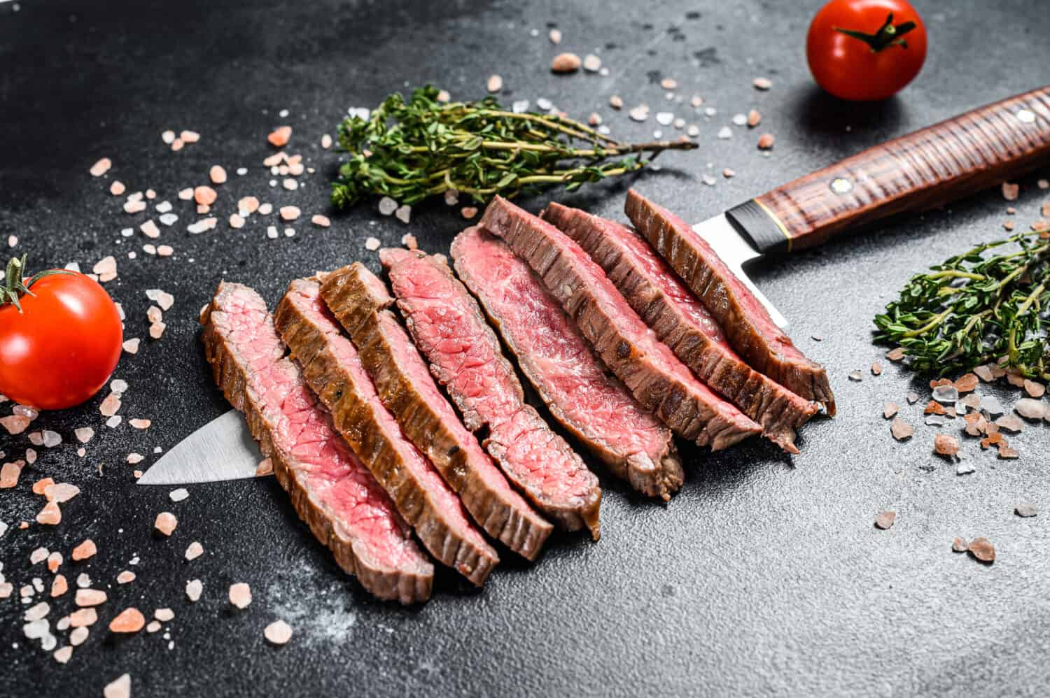 Grilled and sliced flat iron rare steak. Marble beef meat. Black background. Top view