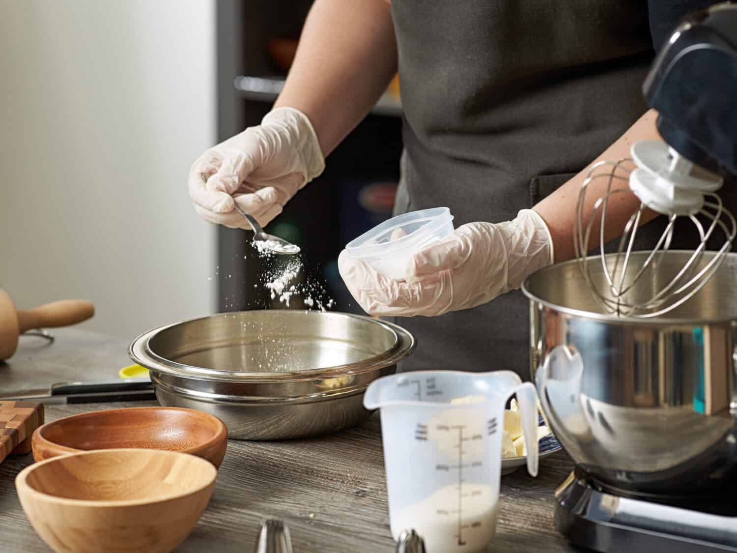 A closeup of a pastry chef adding flour or baking powder to a mixer bowl to make a dessert dough.