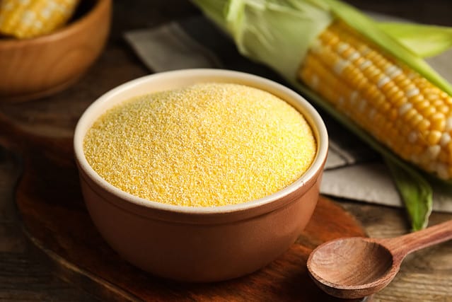 Cornmeal in bowl on wooden table, closeup
