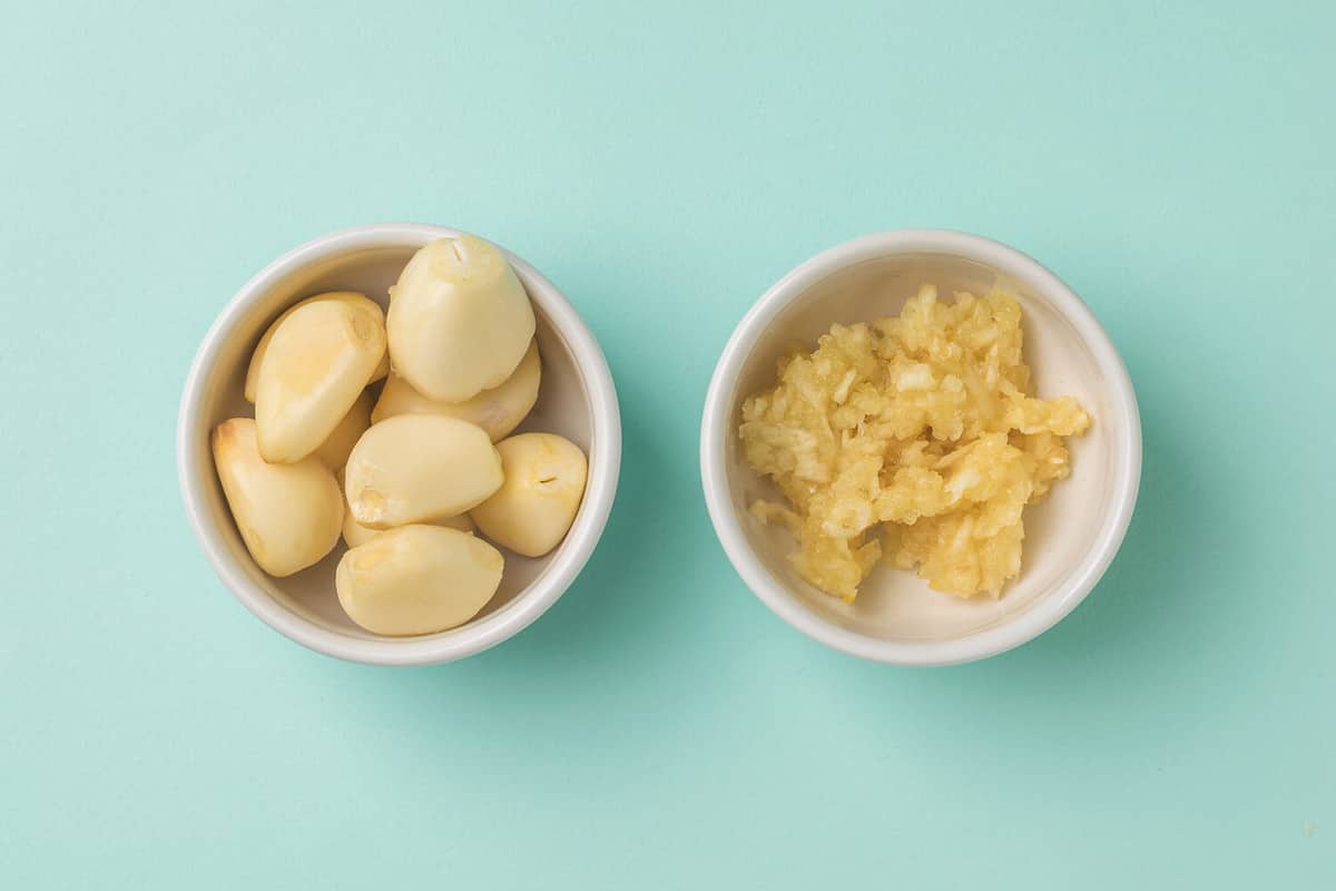 Garlic cloves and mashed garlic in white bowls on a blue background. A popular spice for the kitchen.