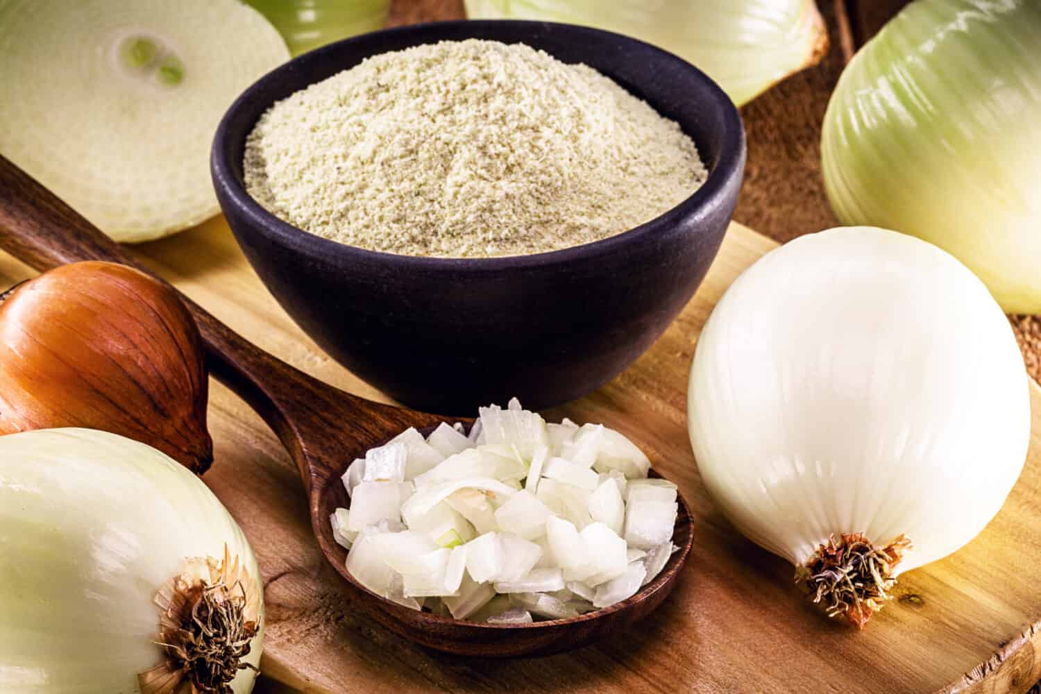 wooden spoon with sliced ​​onion and crushed into pieces to be used as seasoning, with powdered onion in the background, rustic kitchen