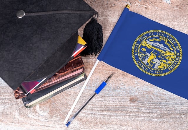 Black graduation hat on books next to Nebraska flag, education concept, top view