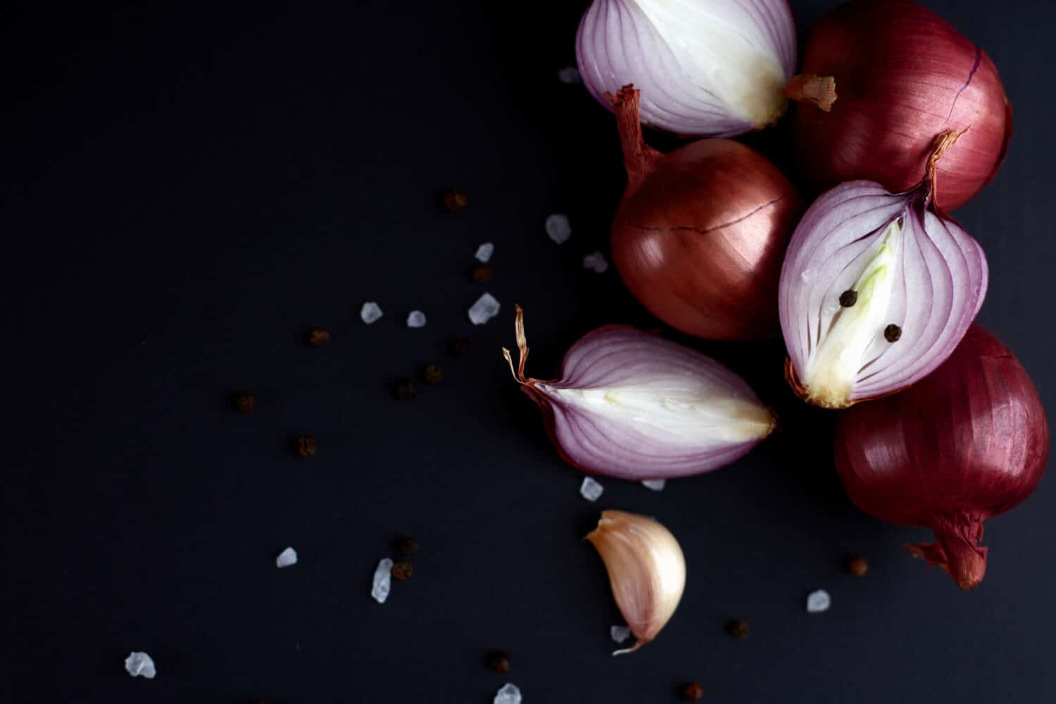 Red onion on black background Whole and sliced onions, salt, garlic and spices. Flat lay, copy space