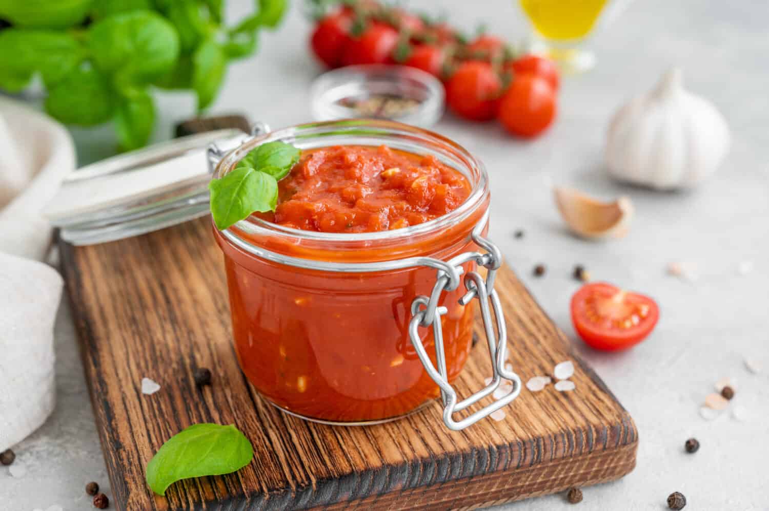 Traditional Italian marinara sauce in a jar on a concrete background with spices and ingredients. Copy space