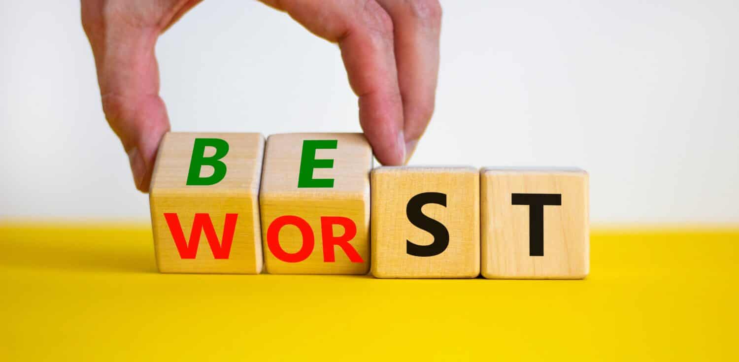 Best or worst symbol. Businessman turns wooden cubes and changes the word best to worst. Beautiful yellow table, white background, copy space. Business and best or worst concept.