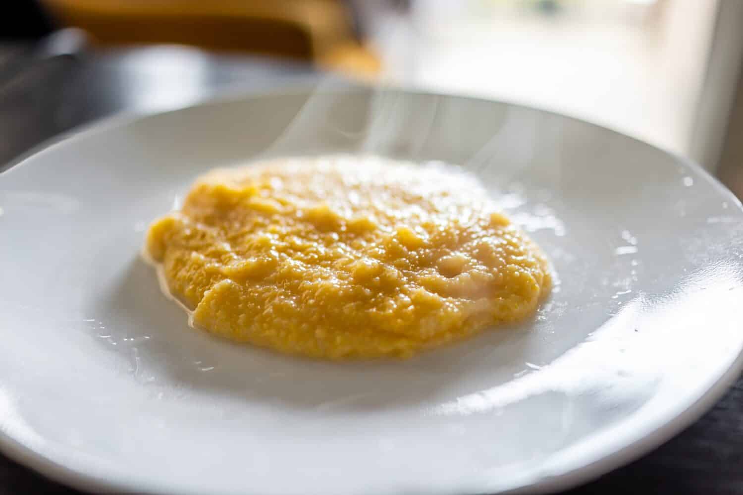 Cooked yellow southern american corn grits on plate as breakfast porridge with hot steam rising and texture of healthy cereal