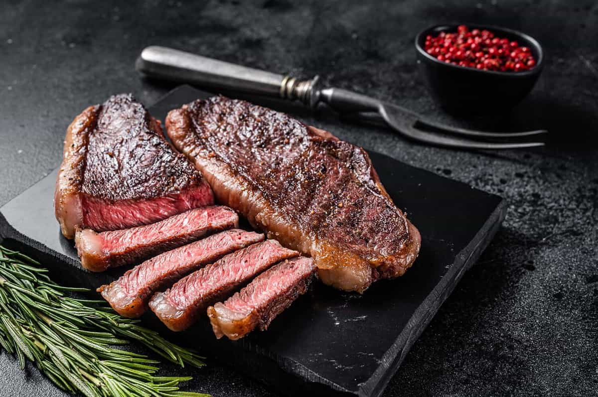 Grilled top sirloin or cup rump beef meat steak on marble board. Black background. Top view