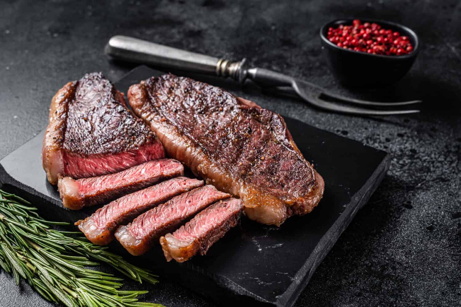 Grilled top sirloin or cup rump beef meat steak on marble board. Black background. Top view