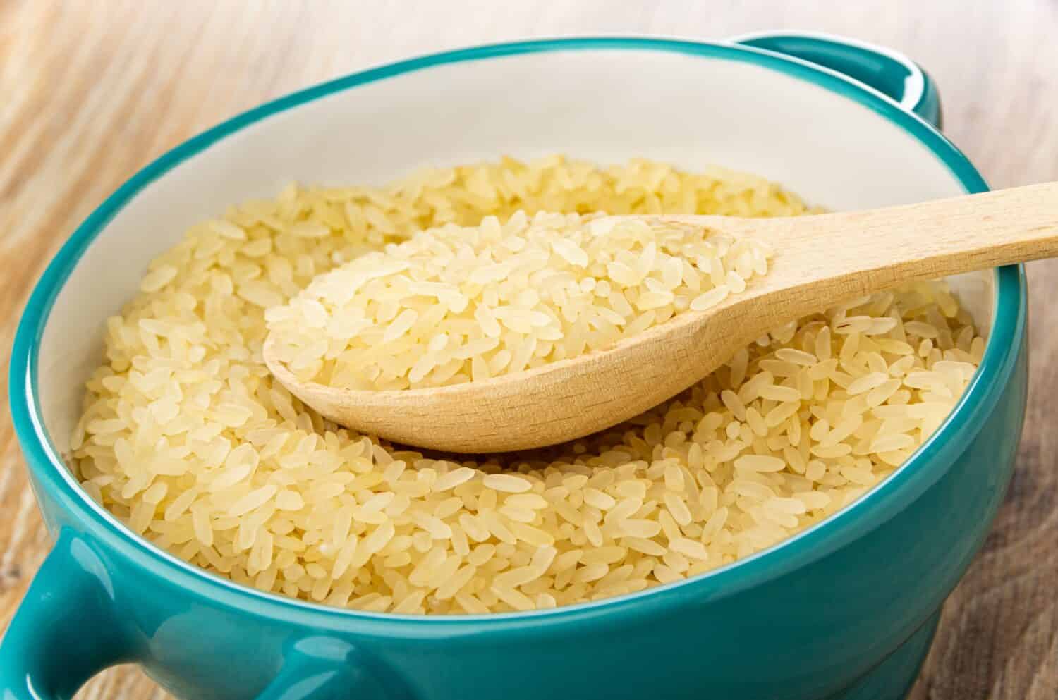 Wooden spoon with parboiled rice in blue glass bowl