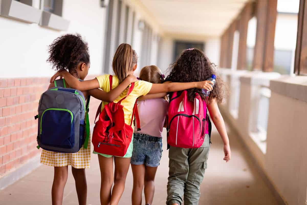  Photo of a group of elementary school pupils with arms over each others shoulders walking from a busy day at school.