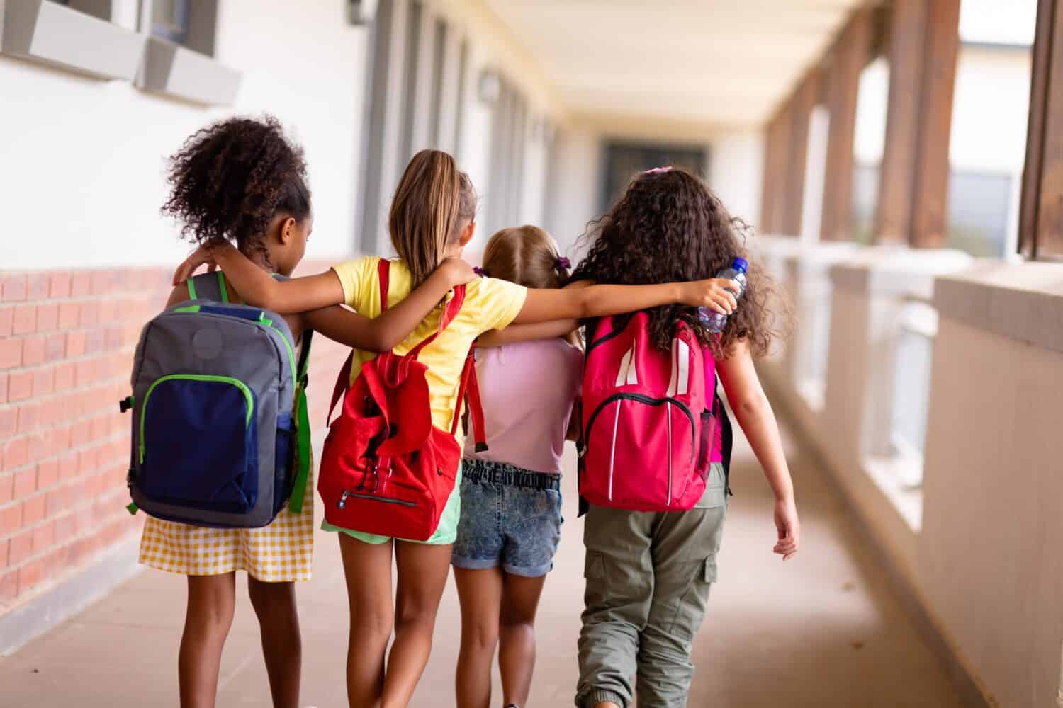 A group of young students arms over each others shoulders walking through the school's hallway.