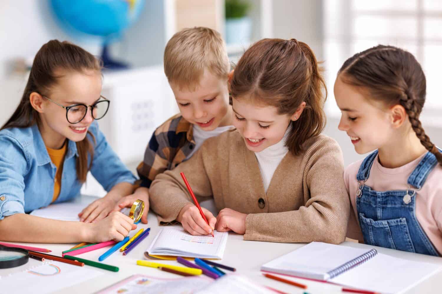 Smart kids pupils writing down data into notebook while communicating with classmates during lesson at school in daytime