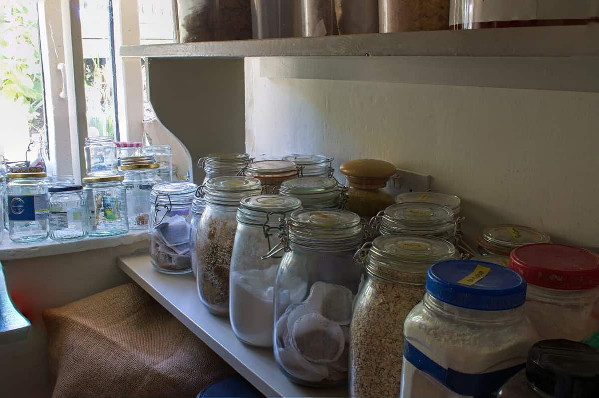 Glass jars full of provisions in a country pantry. Kilner jars and tubs of all shapes and sizes in a windowed country larder. Home made food stuffs and supplies. Country cottage rustic cooking.