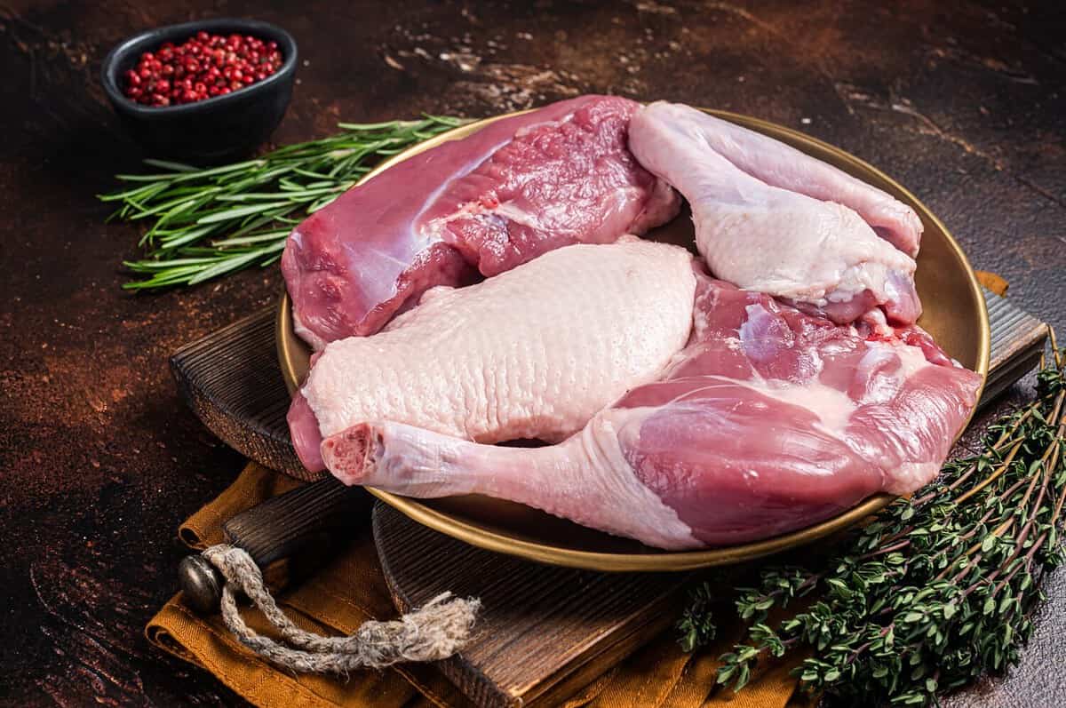 Fresh duck meat parts, raw breast steak, legs, wings in a plate with herbs. Dark background. Top view.