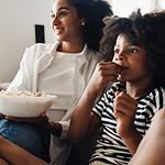 African american mom and son in casual wear eating popcorn and watching TV while sitting on sofa at home