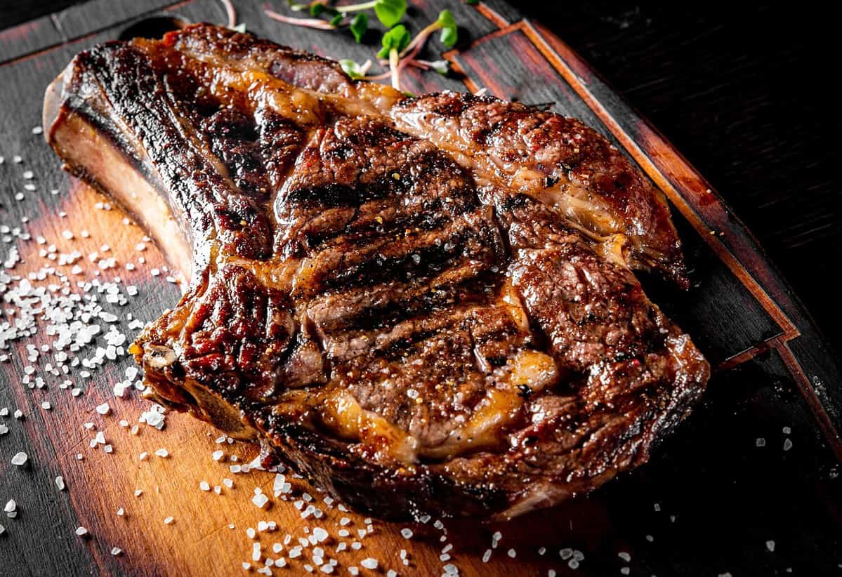 Grilled Ribeye Steak on bones on wooden board, prime cowboy steak on dark background