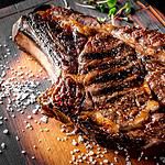 Grilled Ribeye Steak on bones on wooden board, prime cowboy steak on dark background