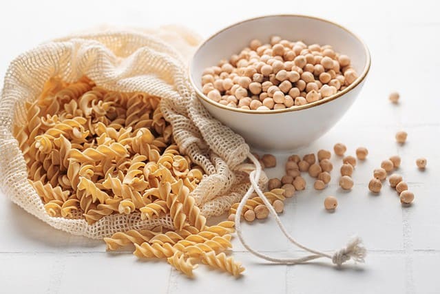 Chickpea ben fusilli pasta on a white tile background. Bag with raw pasta and bowl with chickpea beans. Gluten free pasta.