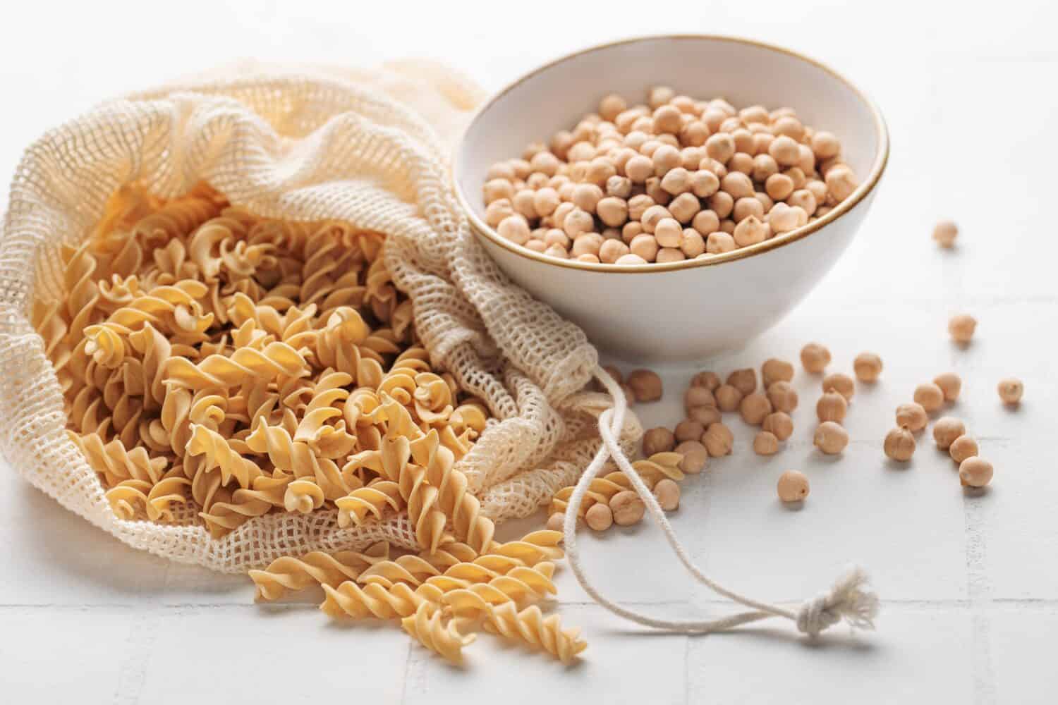 Chickpea ben fusilli pasta on a white tile background. Bag with raw pasta and bowl with chickpea beans. Gluten free pasta.